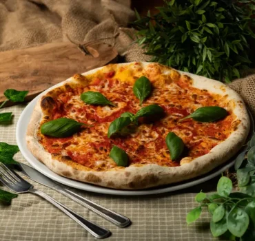 Na zdjęciu widoczna jest pizza Margherita z sosem pomidorowym, roztopionym serem i świeżymi liśćmi bazylii, ułożona na okrągłym talerzu.