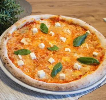 Na zdjęciu znajduje się pizza margherita z dodatkiem świeżej bazylii i kostek sera.