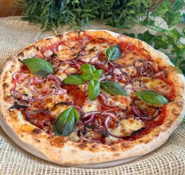 Na grafice widoczna jest pizza z czerwoną cebulą, serem i świeżymi liśćmi bazylii na wierzchu.