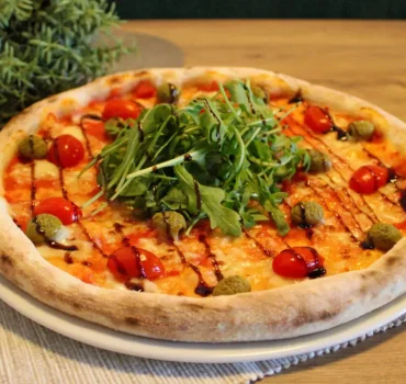 Pizza z rukolą, pomidorkami koktajlowymi, zielonymi oliwkami i polewą balsamiczną.